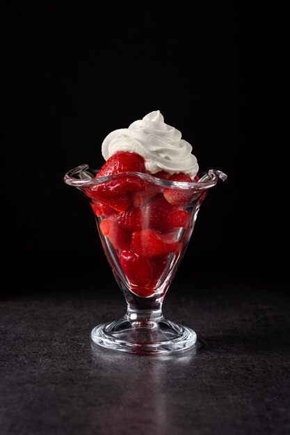 Fragole e panna montata in un bicchiere di gelato su sfondo nero