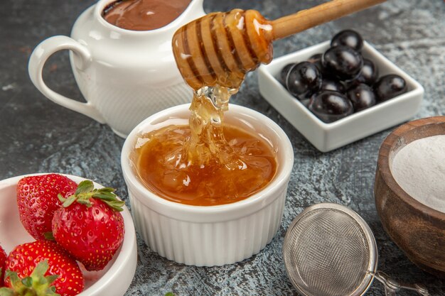 Fragole fresche di vista frontale con miele sul cibo dolce gelatina di frutta superficie scura