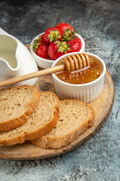 Fragole fresche di vista frontale con pane e miele sulla gelatina dolce di frutti di superficie scura