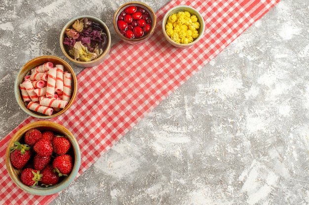 Fragole fresche di vista superiore con le caramelle sulla frutta dolce della caramella di superficie bianca