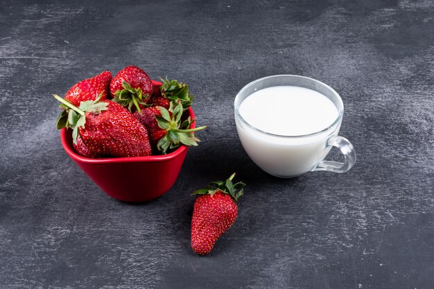 fragole in ciotola e altri intorno con una tazza di latte sul tavolo scuro