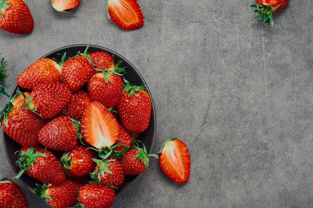 Fragole mature fresche e mezza bacca in un piatto su un tavolo grigio vista dall'alto con spazio per la copia Bacca succosa stagionale