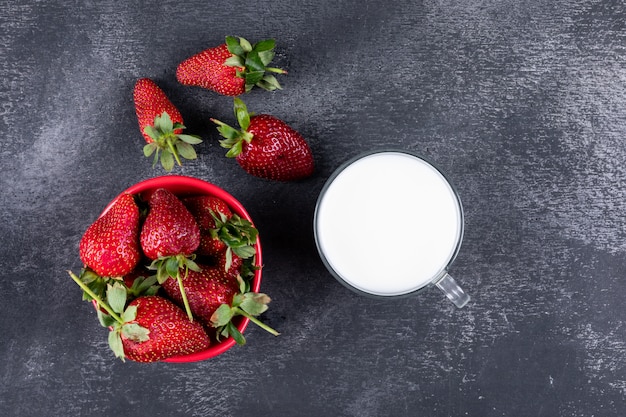 Fragole piatte laici in ciotola e altri intorno con una tazza di latte sul tavolo scuro