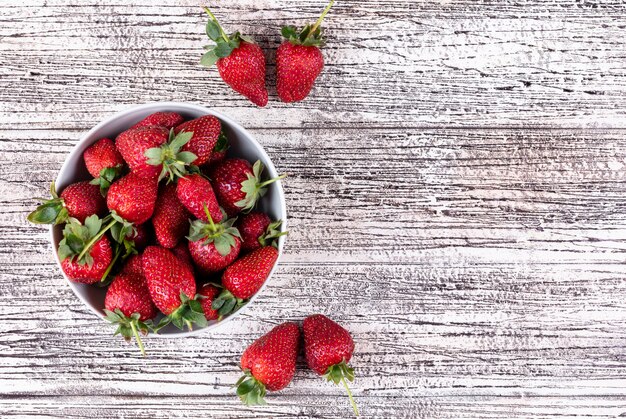 Fragole piatte laici in ciotola e altri intorno sul tavolo di legno chiaro