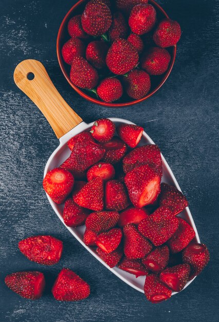 Fragole piatte laici in ciotole sul tagliere e tavolo scuro.