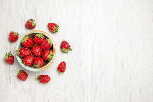 Fragole rosse fresche di vista superiore all'interno del piatto sullo scrittorio bianco