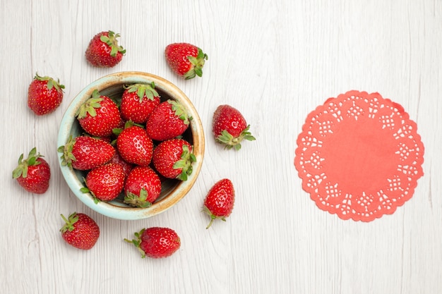 Fragole rosse fresche di vista superiore all'interno del piatto sullo scrittorio bianco