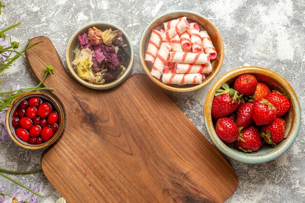 Fragole rosse fresche di vista superiore con i fiori sulla caramella rossa di frutti di bosco di superficie bianca