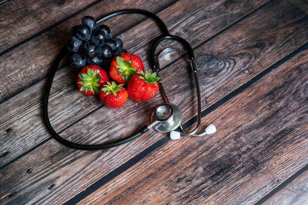 Fragole rosse scozzesi e uva nera con lo stetoscopio sulla parte superiore del tavolo in legno. Cibo sano e medico concettuale.