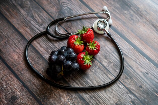 Fragole rosse scozzesi e uva nera con lo stetoscopio sulla parte superiore del tavolo in legno