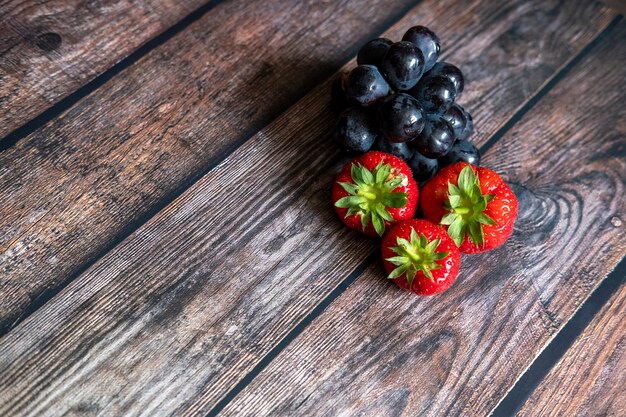 Fragole scozzesi fresche e uva nera in cima alla tavola di legno