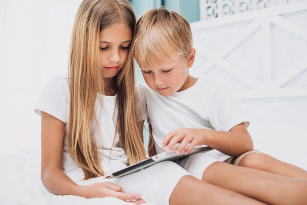 Fratelli di vista frontale stare a letto mentre guardando tablet
