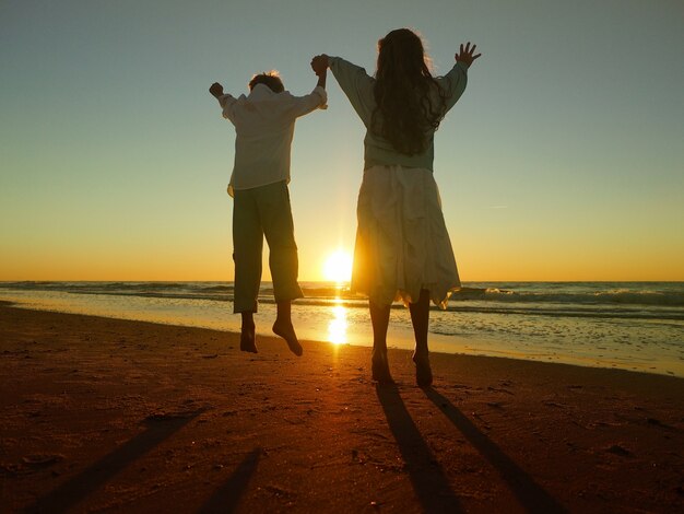 Fratelli germani che saltano in spiaggia circondati dal mare durante il tramonto