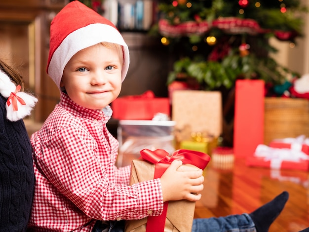 Fratello felice con un regalo di Natale si siede sul pavimento