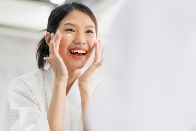 Freschezza attraente donna asiatica viso pulito acqua fresca con cura guarda allo specchio in bagno casa sfondo