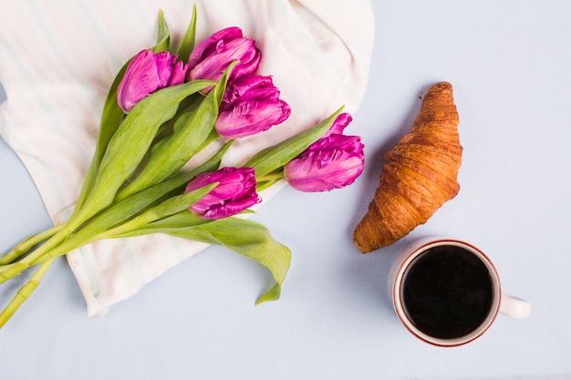 Freschi tulipani viola; tazza di tè e croissant su sfondo bianco