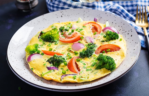 Frittata con broccoli, pomodori e cipolle rosse sul tavolo scuro. Frittata italiana con verdure.