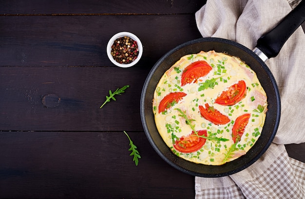 Frittata con pomodori, prosciutto e cipolla verde sul tavolo scuro