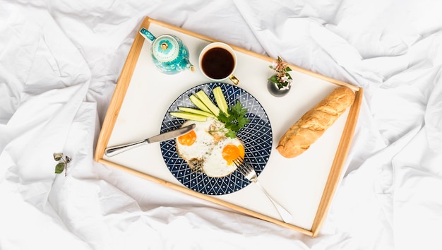 Frittata di uova fritte con pane e tè sul vassoio di legno sopra il letto