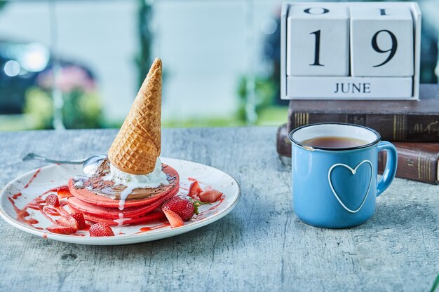 Frittelle con cono gelato, fragole e tè caldo sulla superficie del calendario e dei libri