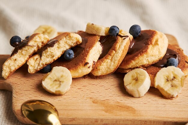 Frittelle con salsa al cioccolato, frutti di bosco e banana su un piatto di legno