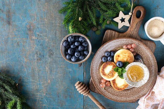 Frittelle di ricotta Cheesecake con miele di ribes e mirtilli su sfondo blu Cibo dolce per la colazione per il nuovo anno