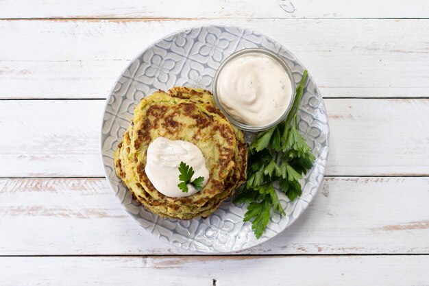 Frittelle di zucchine con salsa allo yogurt sul tavolo di legno bianco