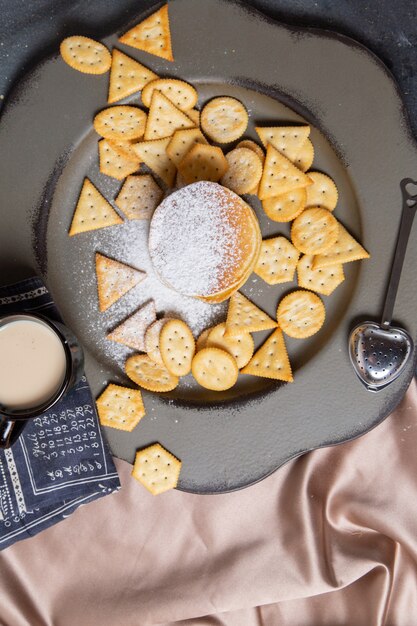 Frittelle e cracker con vista in lontananza superiore con tazza di latte nera sullo sfondo grigio cibo croccante per la colazione