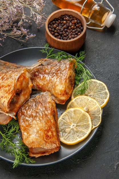 Frittura di pesce vista dal basso con fette di limone su piatto pepe nero in una bottiglia di olio di ciotola di legno su sfondo scuro