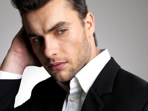 Fronte del primo piano di un giovane uomo d'affari di modo in pose casuali del vestito nero allo studio