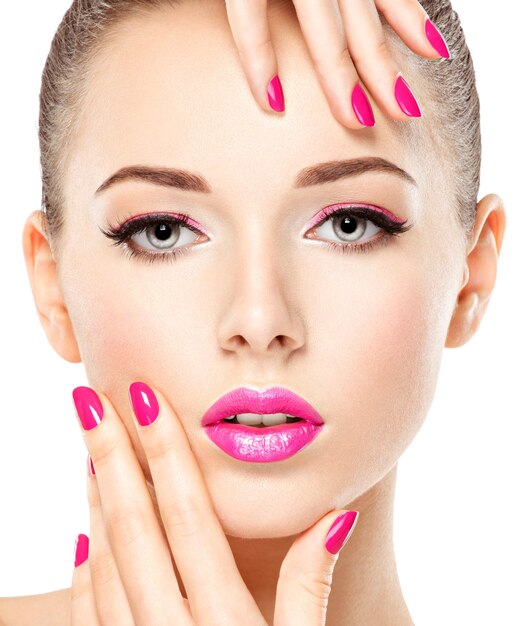 Fronte del primo piano di una bella ragazza con il trucco degli occhi rosa e unghie rosa brillante. Modello di moda in posa sul muro bianco