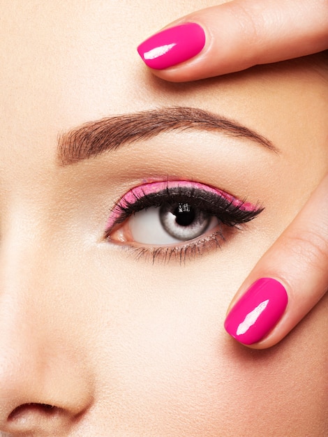 Fronte della donna del primo piano con le unghie rosa vicino agli occhi. Unghie con manicure rosa