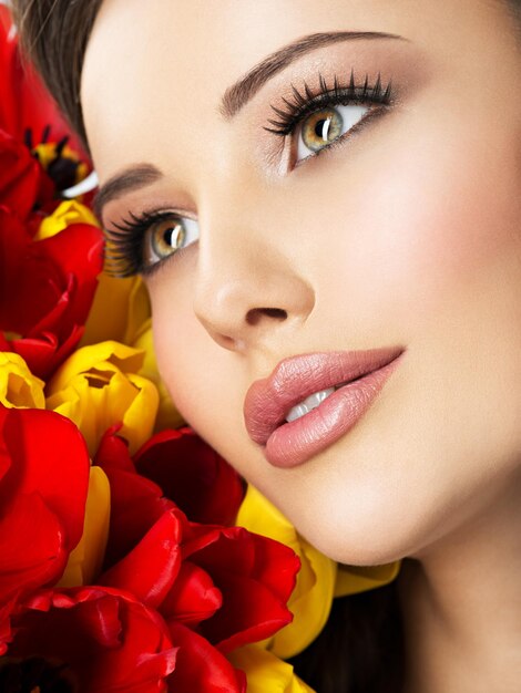 Fronte di bellezza del primo piano della giovane donna con i fiori. Modello attraente con tulipani rossi e gialli