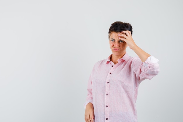 Fronte femminile che sfrega in camicia rosa e che sembra triste, vista frontale.