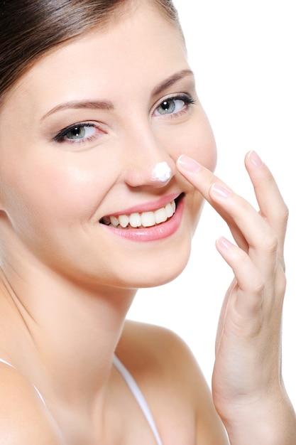 Fronte femminile sorridente di bellezza con goccia di crema cosmetica sul naso
