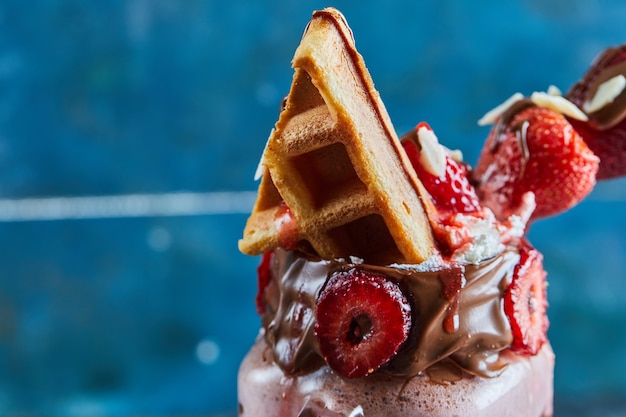 Frullato di fragole con minuscoli waffle, cioccolato e fette di fragole nella superficie blu scuro