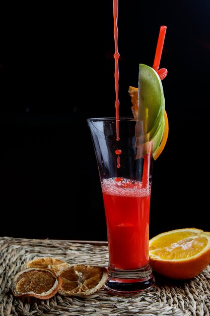 Frullato di frutta rossa vista laterale con tubuli per bevande e limone essiccato e gocce in tovaglioli di servizio