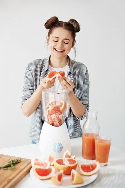 Frullato di rinfresco di miscelazione sorridente del pompelmo della disintossicazione della ragazza graziosa sopra la parete bianca. Concetto di cibo sano.