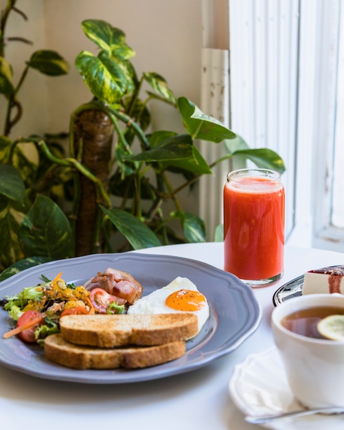 Frullato rosso; colazione e tè sul tavolo bianco vicino alla pianta di epipremnum aureum