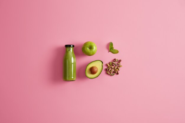 Frullato verde sano a base di mela succosa, avocado, pistacchio e menta. Sfondo roseo. Bevanda fresca e nutriente per una dieta equilibrata. Ingredienti per preparare una bevanda nutriente rinfrescante.
