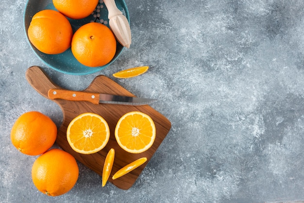 Frutta arancione a fette con arance intere su una tavola di legno.