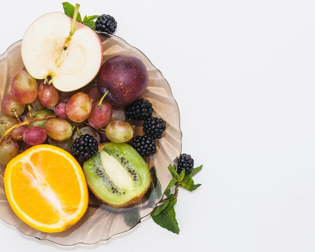 Frutta dimezzata; more e uva nella ciotola su sfondo bianco