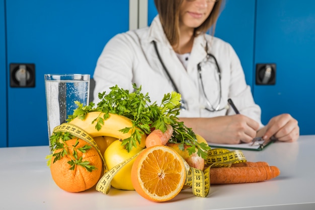 Frutta fresca con nastro adesivo di misurazione davanti al dietista femminile scrivendo su Appunti