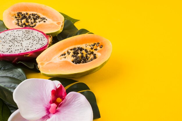 Frutta fresca del papaya e del drago divisa in due con il fiore e le foglie dell&#39;orchidea sul contesto giallo