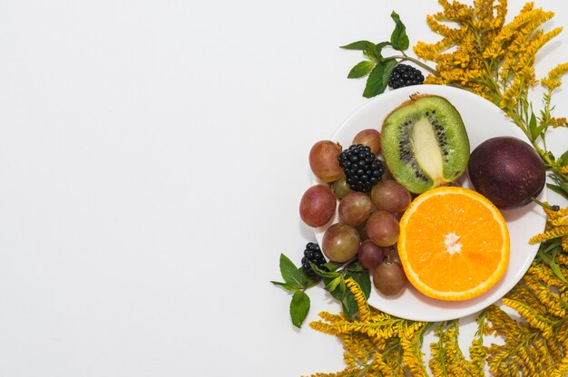 Frutta fresca sul piatto bianco con fiori gialli su sfondo bianco