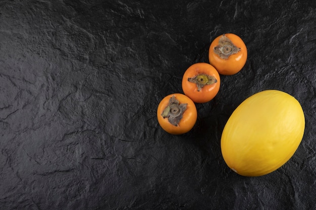 Frutti di cachi maturi e melone delizioso sulla superficie nera