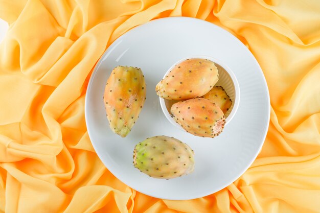 Frutti di cactus in ciotola e piatto su una superficie tessile gialla