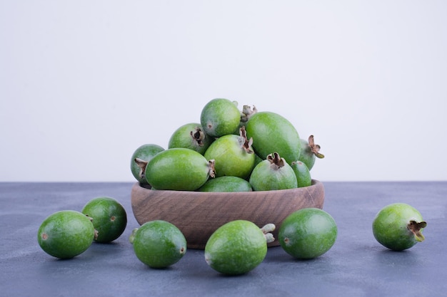 Frutti di feijoa verde in una tazza di legno sul tavolo blu.