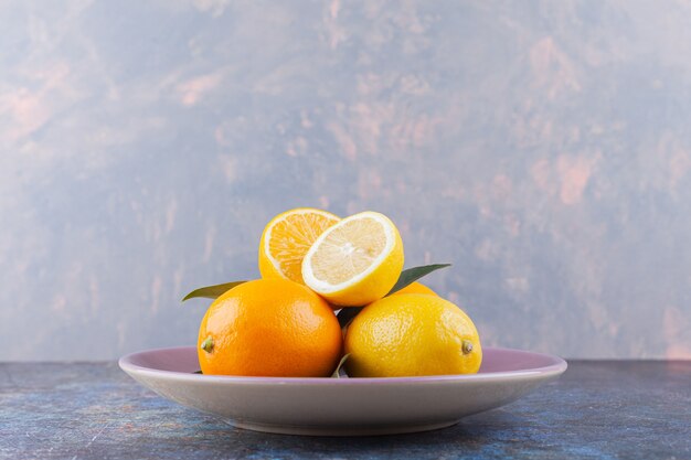 Frutti di limone interi e affettati con foglie poste sul tavolo di pietra.