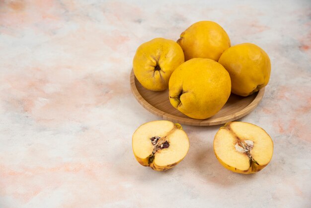 Frutti di mele cotogne fresche affettate e intere sul piatto di legno.